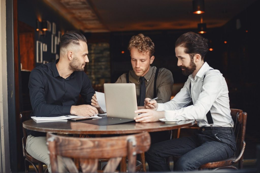 Three businessmen engaged in discussions over a laptop at a table, focusing on operational strategies for industrial business management.