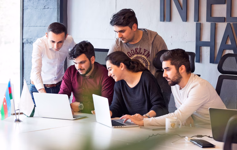 Colleagues collaborating on a project at a conference table, discussing details and reviewing information on laptops, in a modern office setting.