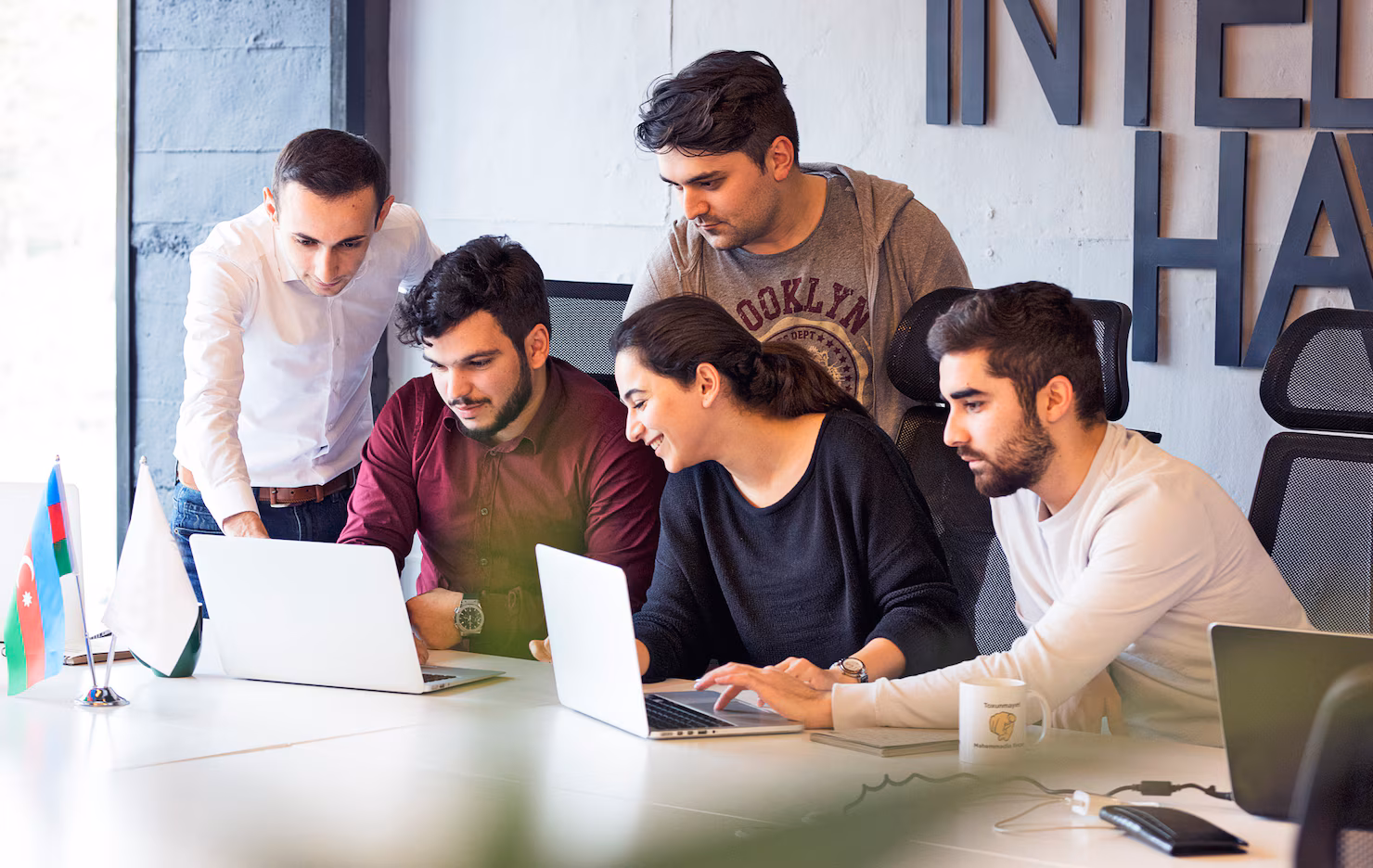 Colleagues collaborating on a project, discussing details over laptops in a modern office setting, reflecting teamwork and training in organizational contexts.