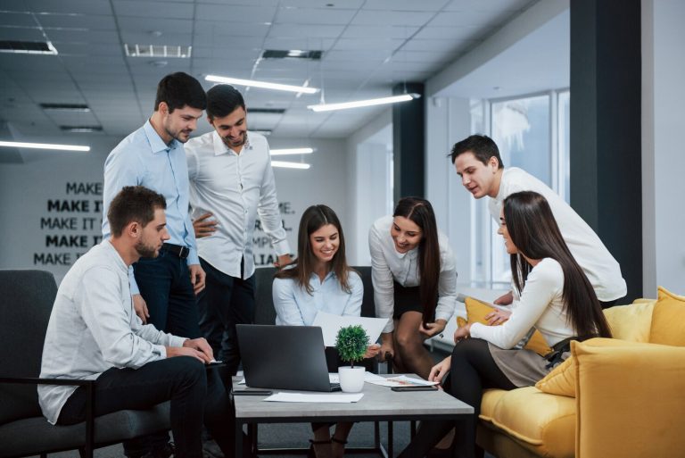 Group of young freelancers collaborating in an office setting, discussing project details around a laptop, emphasizing teamwork and consultation in ERP implementation.